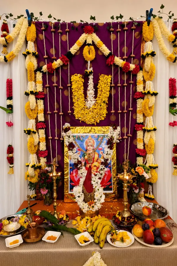 Lakshmi Pooja backdrop with layered flower garlands, brass lamps, fruit and festive offerings